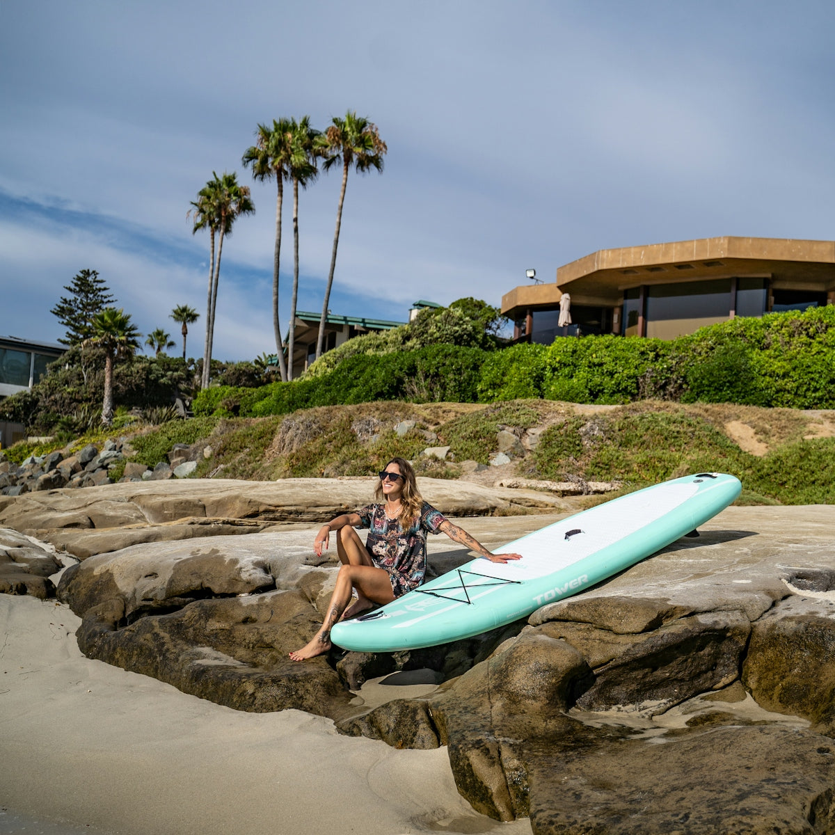 a woman sitting on a rock with a surfboard