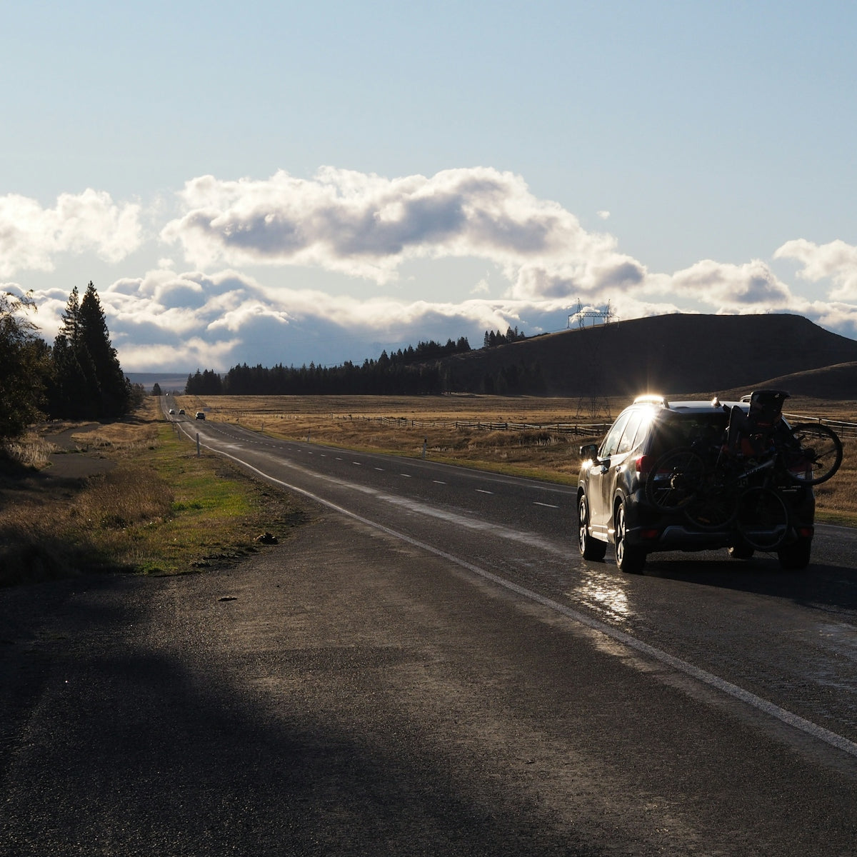 A car travels down a road under the clouds.