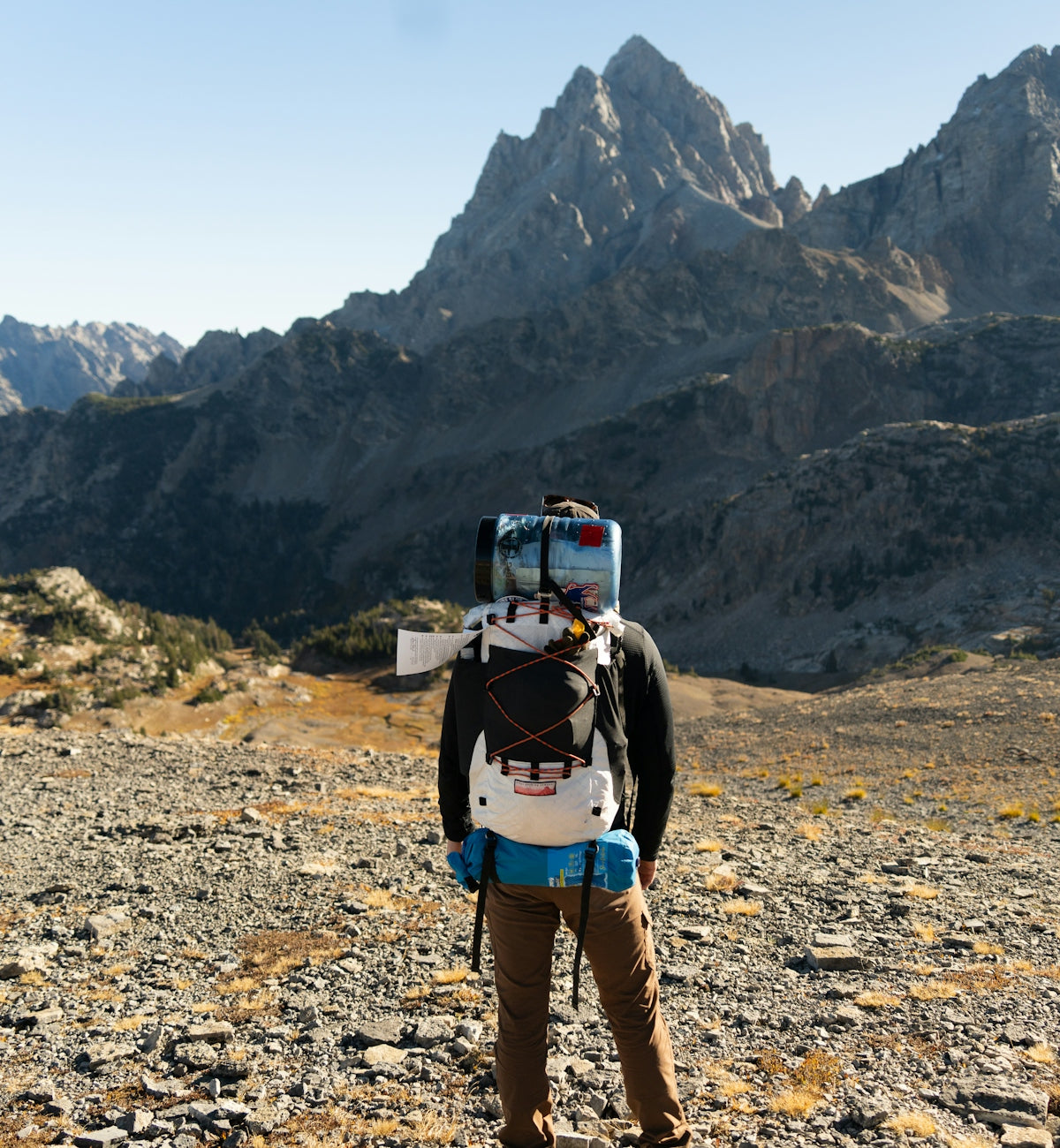Hiker with backpack stands before a mountain range.